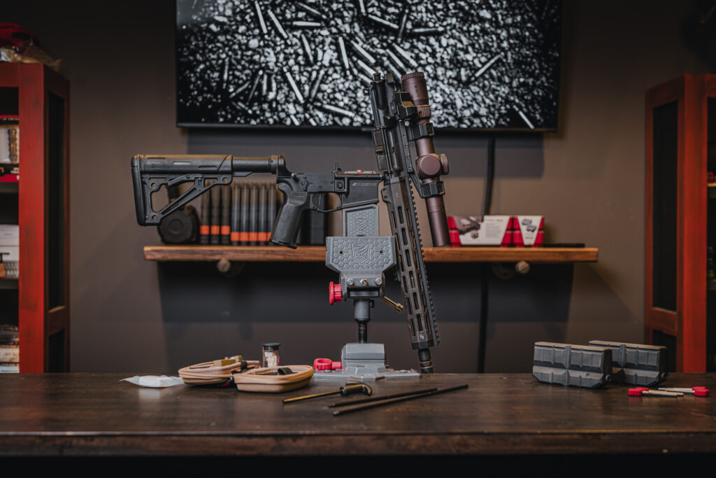 A Real Avid Master Gun Vise securely holding a disassembled firearm on a workbench, showcasing its clamping mechanism and surrounding tools for maintenance and cleaning.